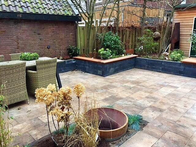 Terras met stenen bestrating, een bakstenen muur en verhoogde plantenbedden.