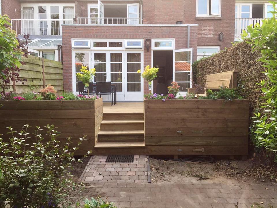 Achtertuin met houten plantenbakken, een trap naar een terras en een bakstenen huis.