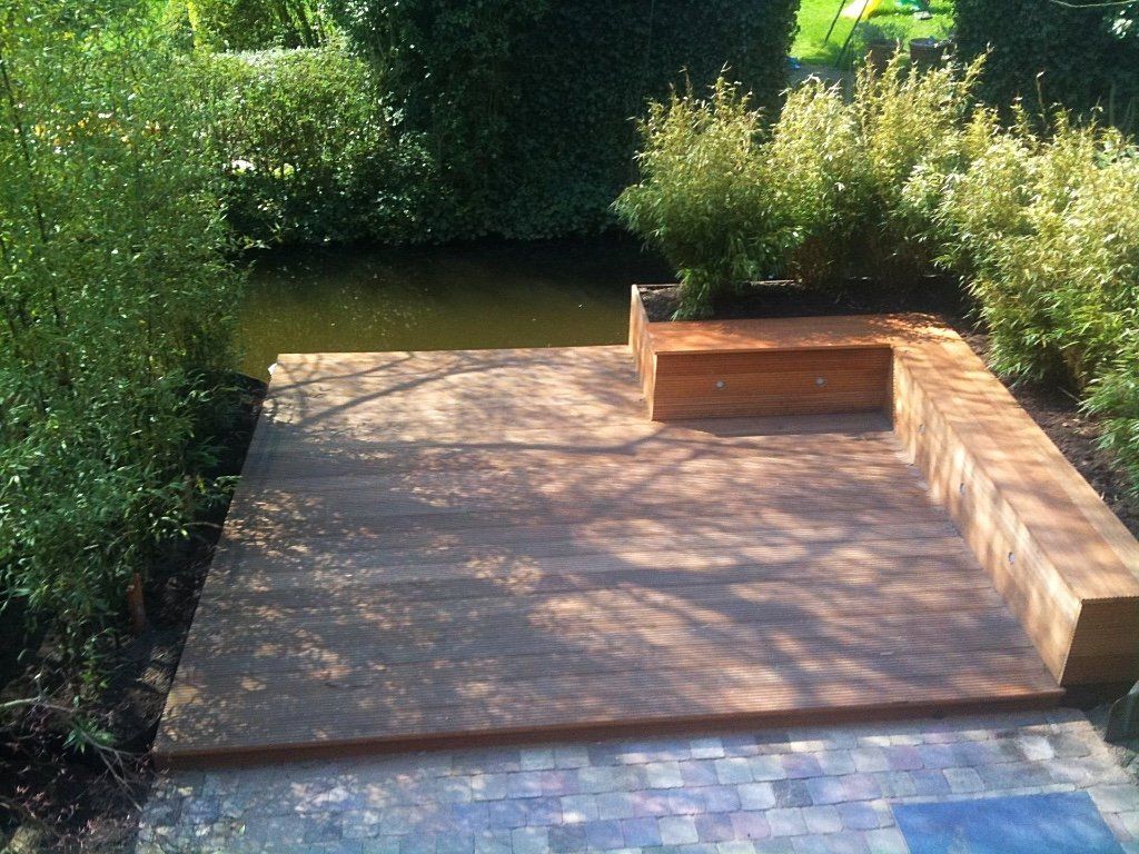 Houten terras met bankje aan het water, omgeven door groen.
