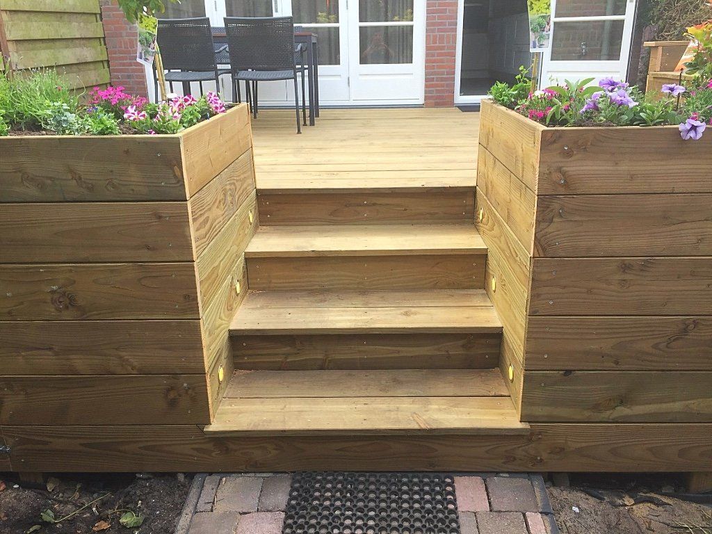 Houten trappen leiden naar een verhoogd terras met bloemperken. De trappen worden geflankeerd door houten wanden.