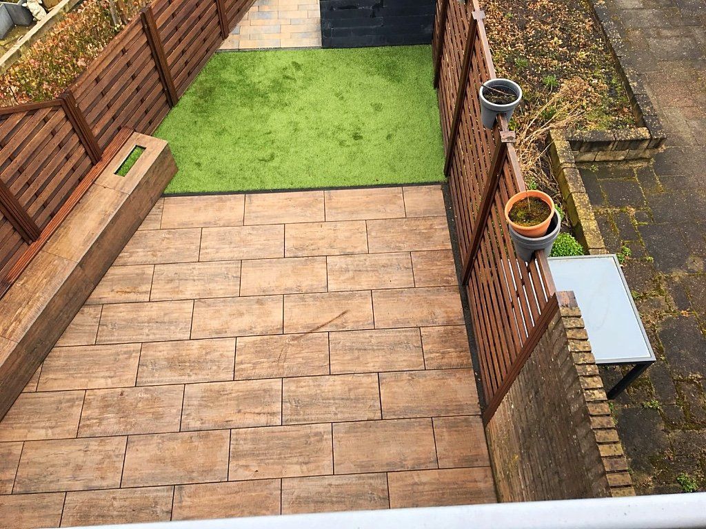 Bovenaanzicht van een kleine achtertuin met een stenen terras, kunstgras en houten schuttingen.
