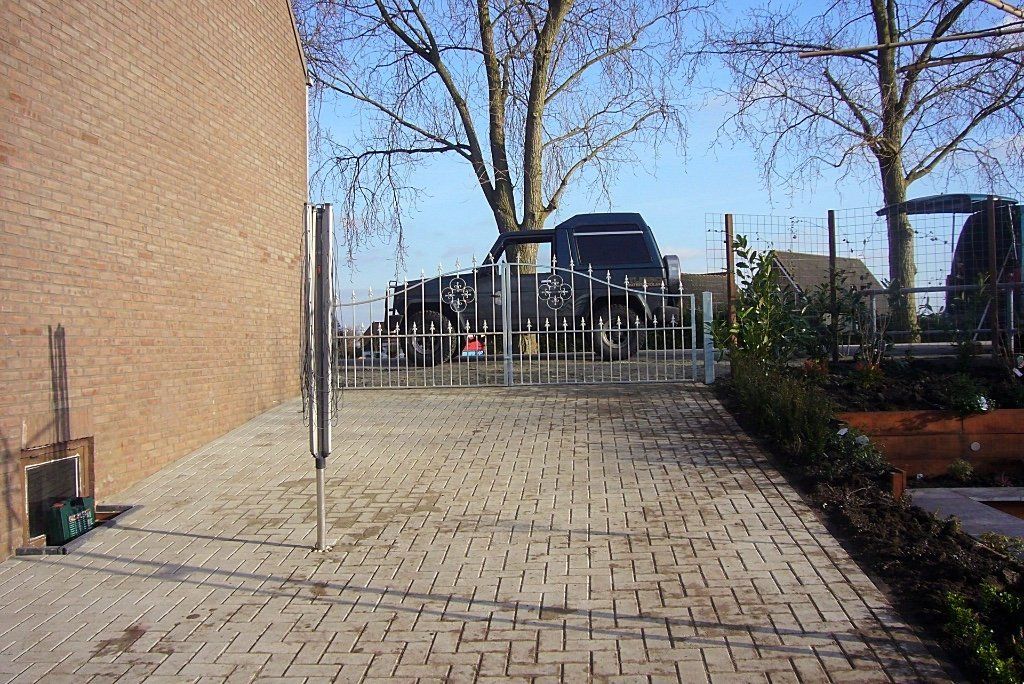 Een stenen pad leidt naar een poort met op de achtergrond geparkeerde voertuigen naast een stenen gebouw.