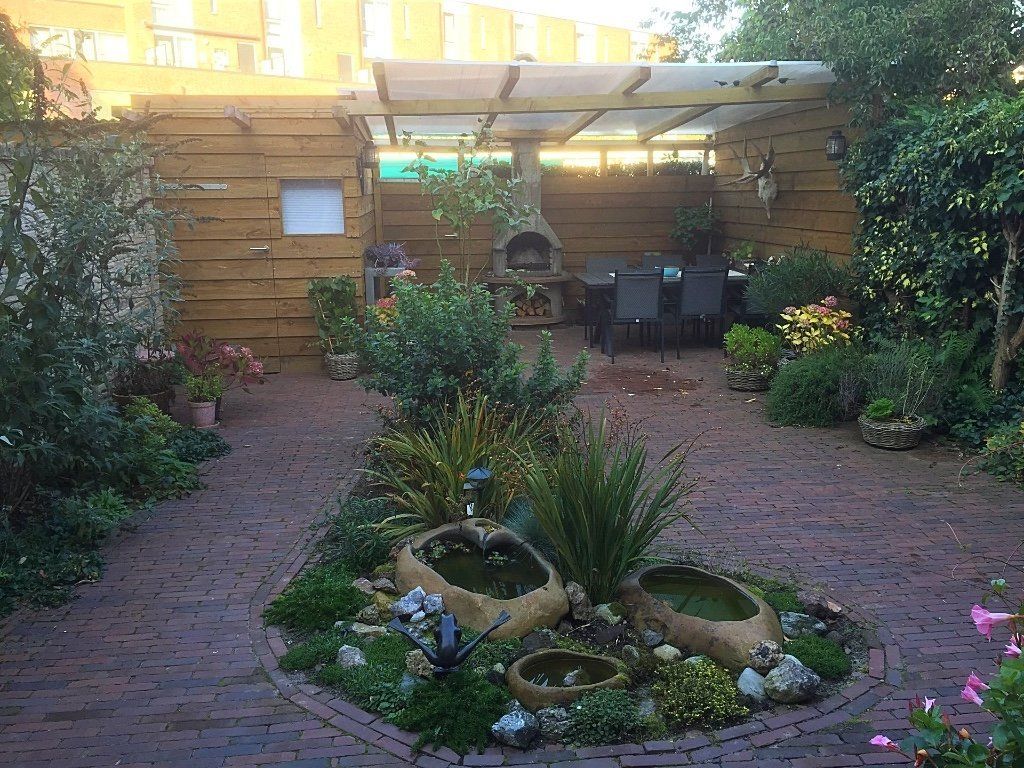 Terras in de achtertuin met een bakstenen pad, een waterpartij en een houten pergola.