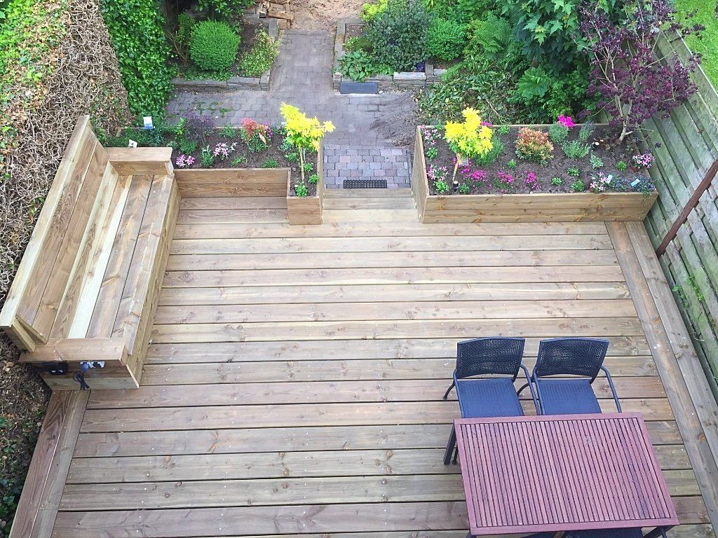 Bovenaanzicht van een houten terras met ingebouwde bank, twee stoelen, een tafel en bloembedden.
