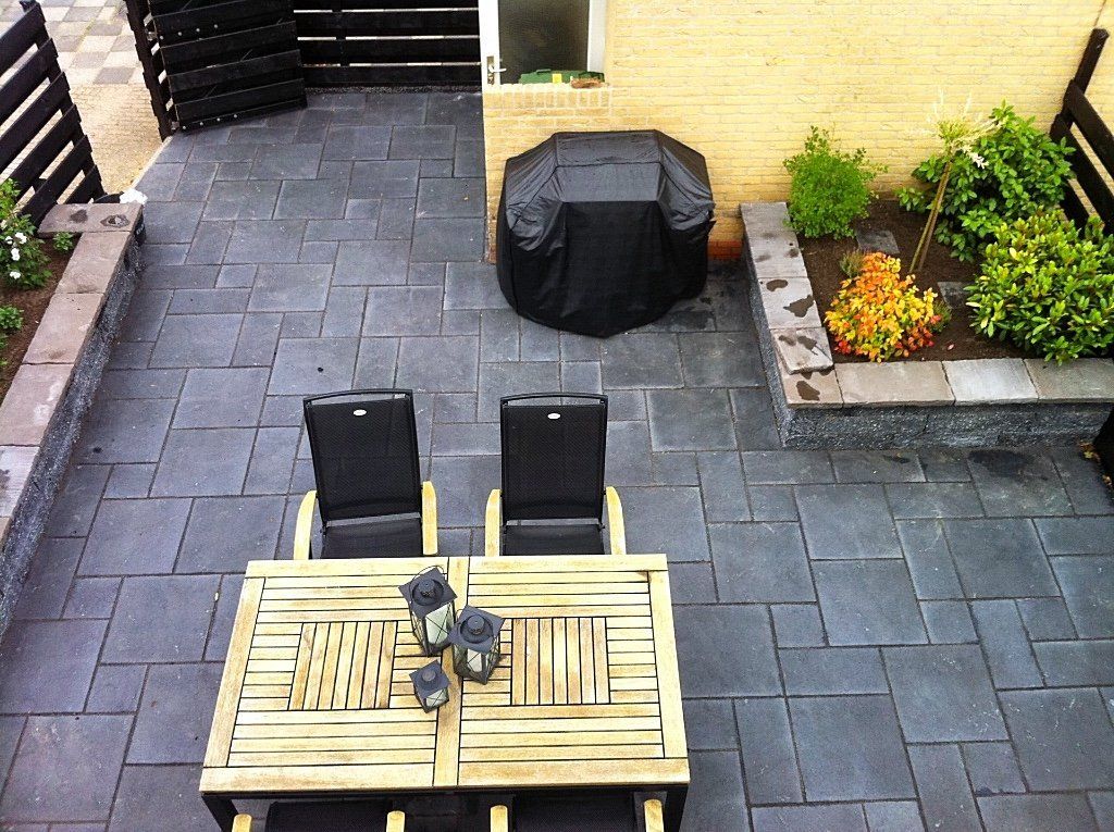 Terras met houten meubels, een barbecue en een kleine tuin met donkergrijze bestrating.