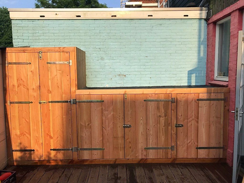 Houten opbergkasten tegen een lichtblauwe bakstenen muur, buiten.