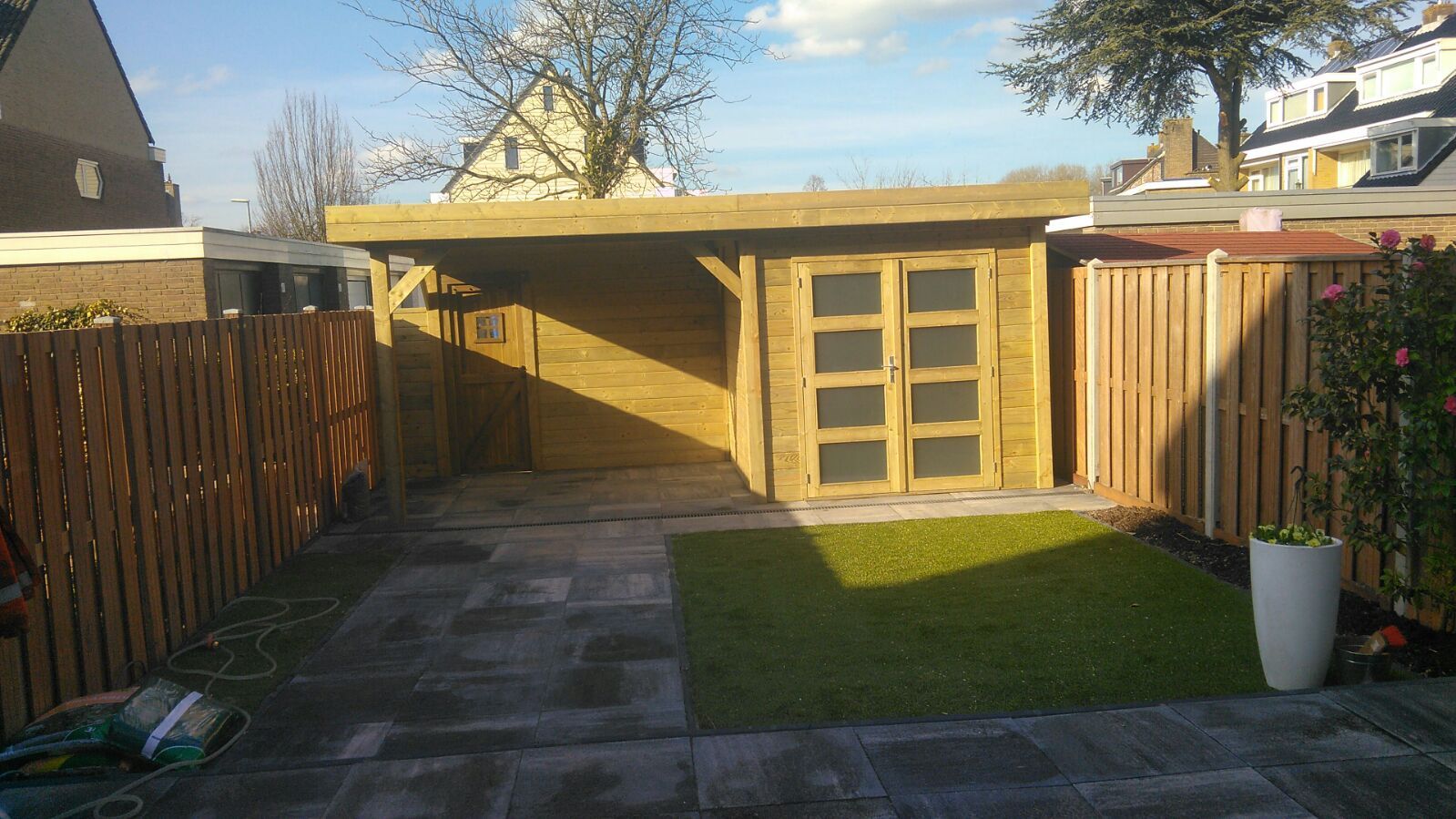 Houten schuur in de achtertuin met gras, omgeven door een schutting.