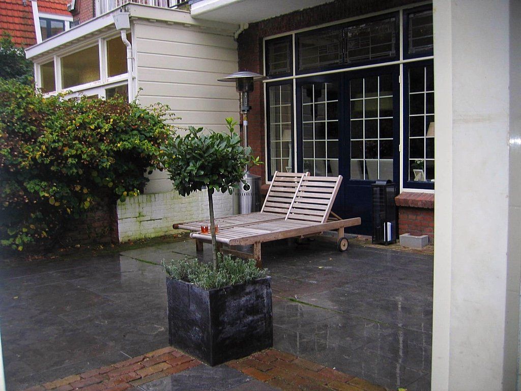 Terras met een ligstoel, donkergrijze natuurstenen tegels en een struik in een vierkante plantenbak.