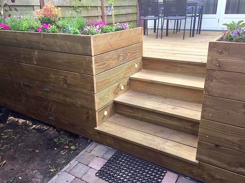Verhoogd houten tuinbed met trap en ingebouwde verlichting, gevuld met bloemen.