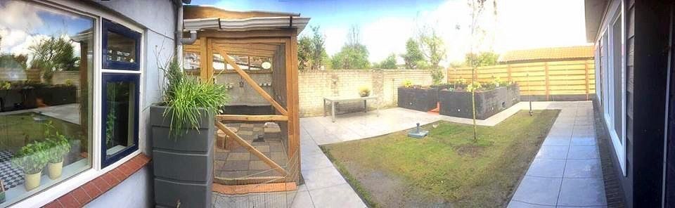 Achtertuin met een verhoogd tuinbed, gras en een houten afscheiding met een raam aan de linkerkant.
