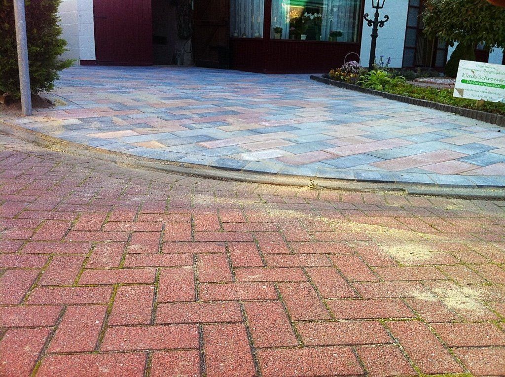Op de voorgrond ligt een rode bakstenen bestrating die leidt naar een kleurrijke bakstenen oprit voor een huis.