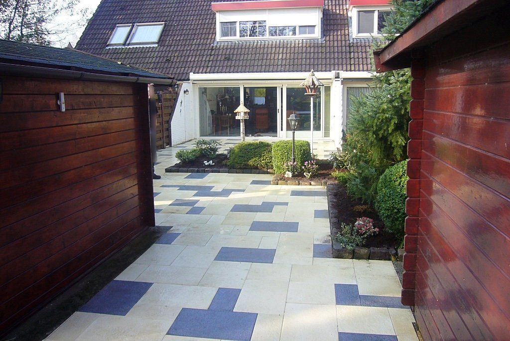 Achtertuin met sierbestrating, omgeven door houten schuurtjes, planten en het huis.
