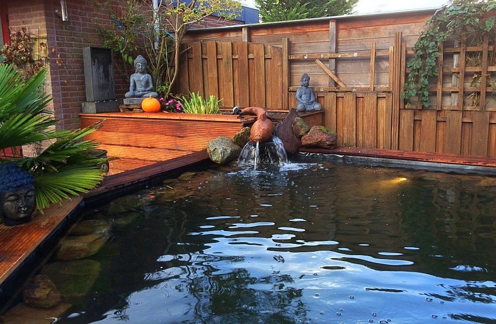 Zen-tuin met een vijver, een houten schutting, een waterfontein en Boeddhabeelden.