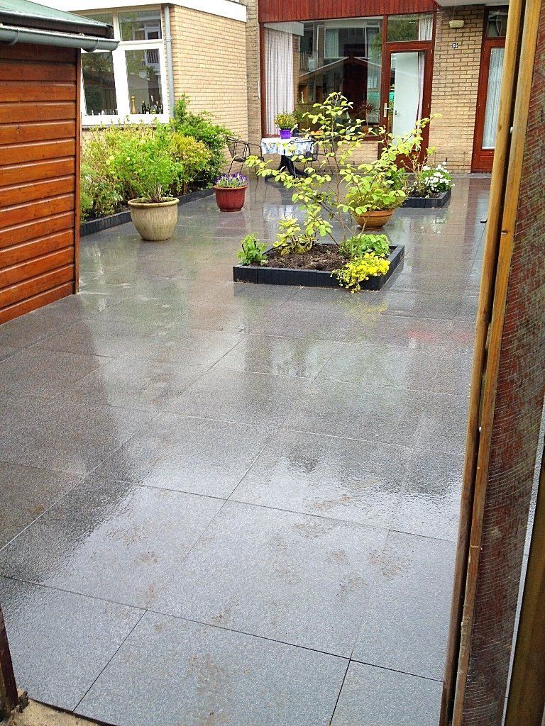 Grijze, betegelde patio met potplanten en bloembedden in een buitenomgeving.