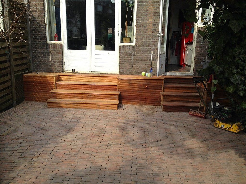 Houten trappen leiden naar witte openslaande deuren op een stenen terras.