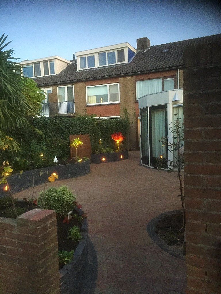 Bakstenen huis met een verzorgde tuin; pad, decoratieve verlichting en donkere hagen.