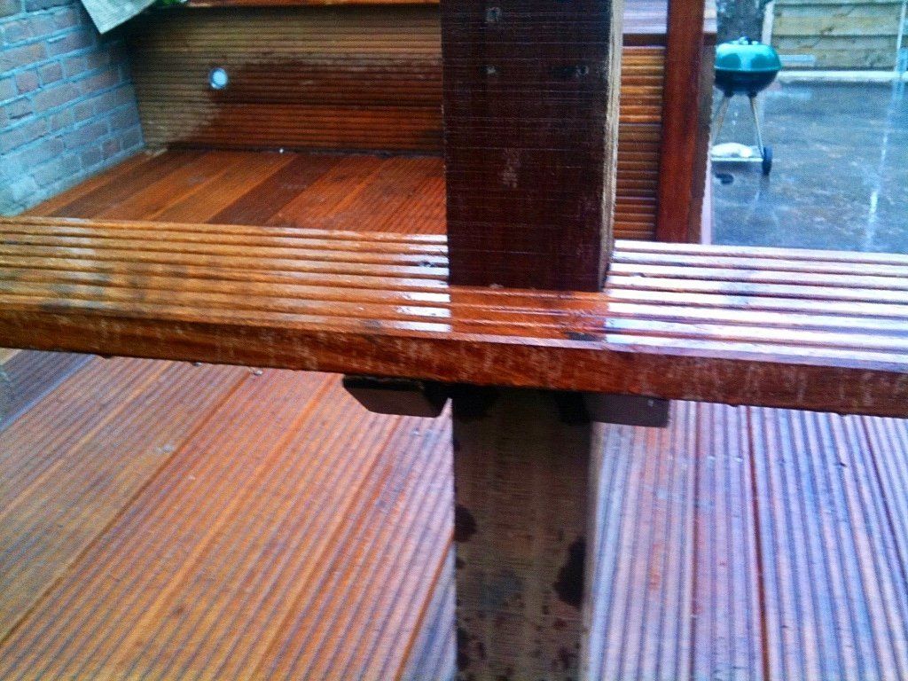 Nat houten terras en pergola in een buitenomgeving. Donker hout is zichtbaar, sommige delen reflecteren de regen.