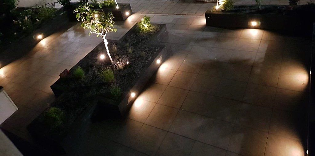 Een buitenruimte 's nachts met ingebouwde verlichting die bomen, planten en stenen oppervlakken verlicht.