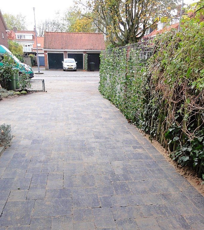 Een stenen oprit leidt naar de garages, omzoomd door een groene heg. Een auto en een bestelbus staan ​​er vlakbij geparkeerd.
