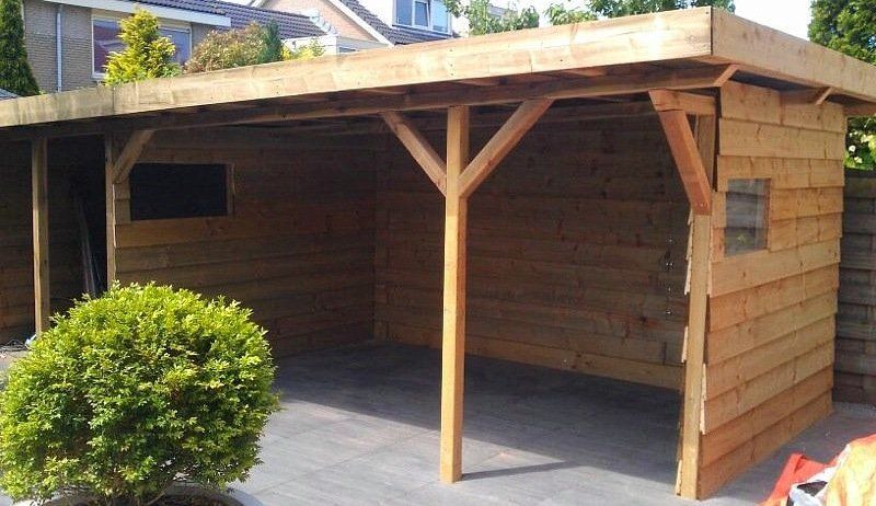 Houten carport met schuur, op een terras, met een groene struik.