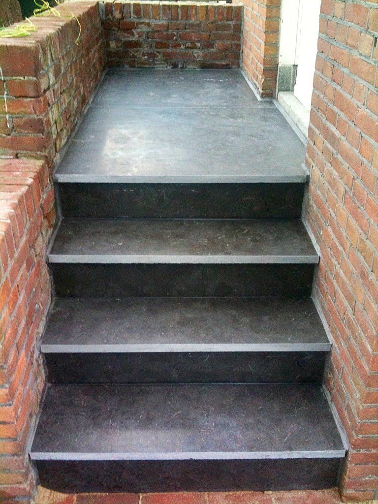Bakstenen trappen die naar een veranda leiden. Donkergrijze treden en verandavloer, met rode bakstenen muren.
