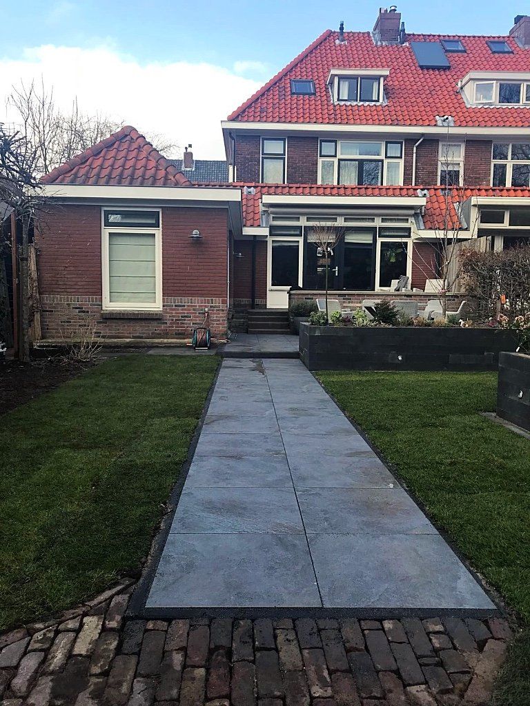 Een bakstenen pad leidt naar een huis met een rood pannendak. Groen gras omringt het pad.