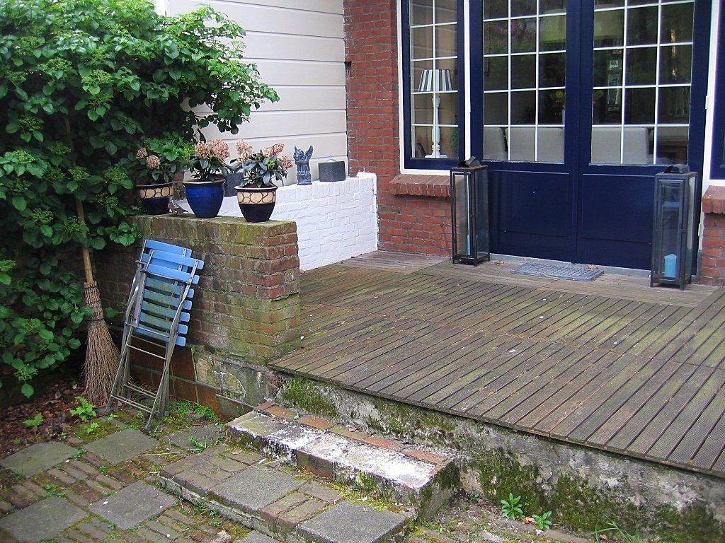 Buitenruimte met blauwe deuren, bloempotten aan de muur, betonnen trappen en blauwe klapstoelen.