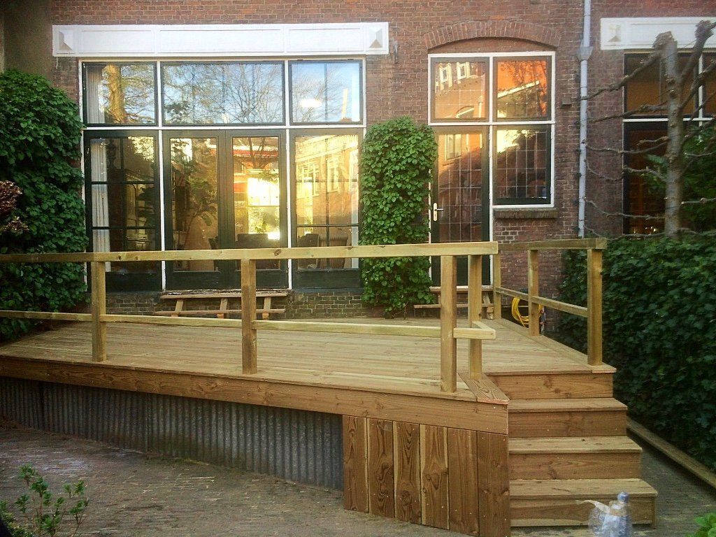 Houten terras met trappen en een leuning voor een gebouw met grote ramen.