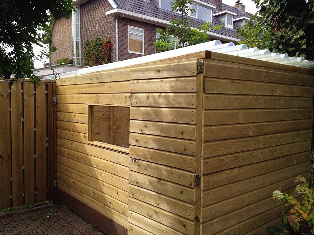 Houten schuur met een klein raam, tegen een schutting en een woonhuis aan.