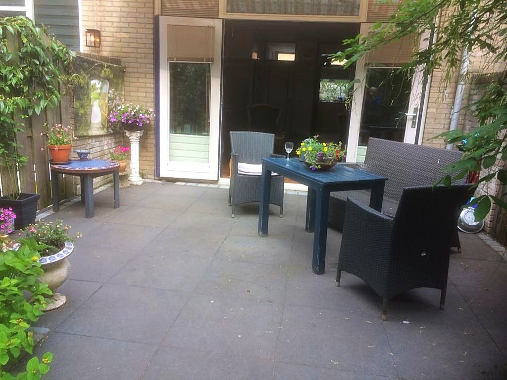 Terras met zwart meubilair, een tafel met drankjes, bloemen en een open deur.