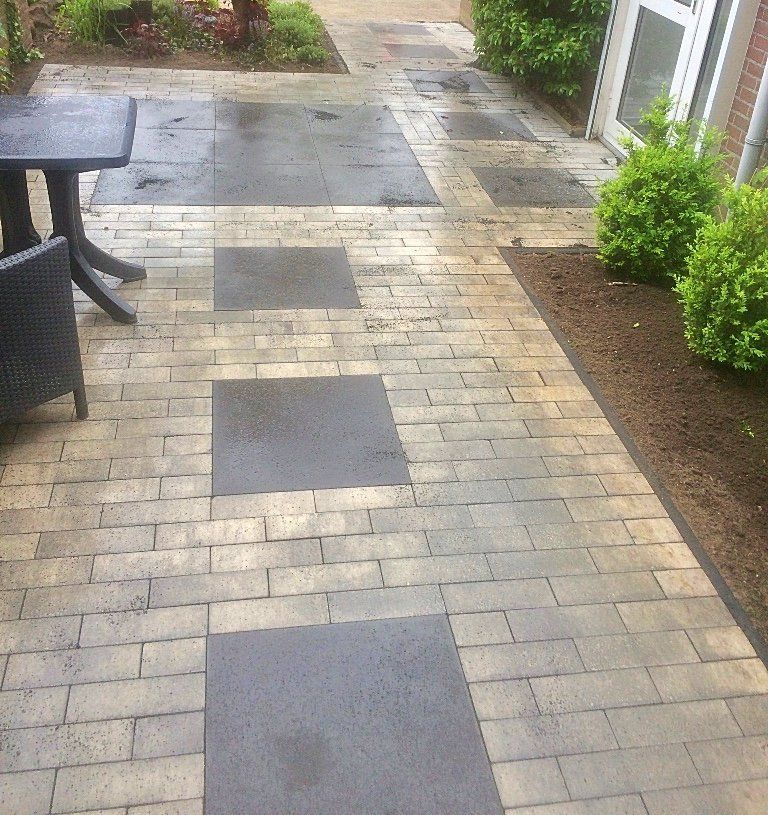 Terras van baksteen en natuursteen met grijze stapstenen, vlakbij een tuintafel en struiken.
