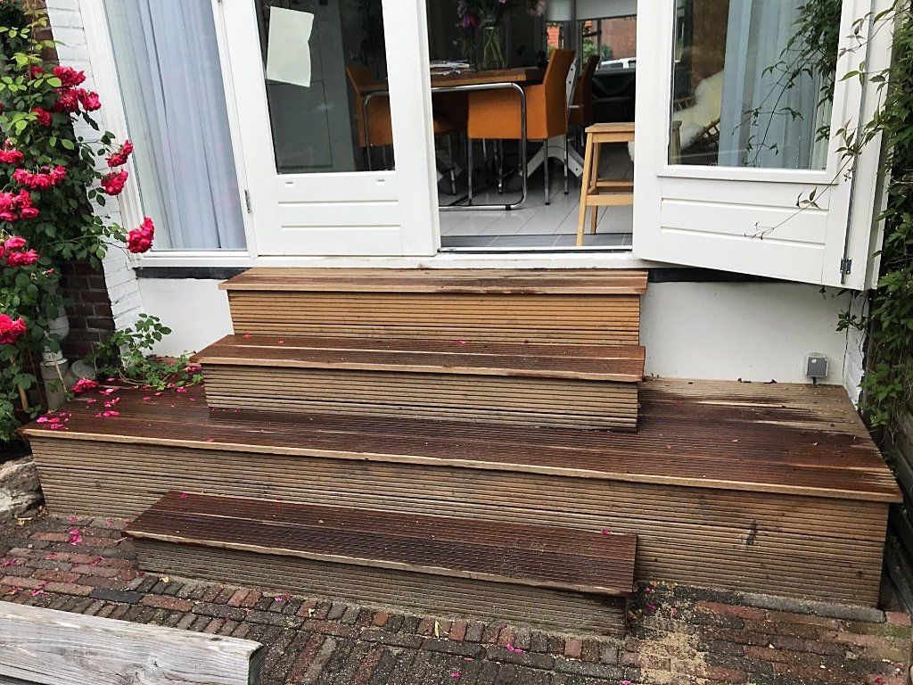 Houten treden die naar een witte deur leiden, met rode rozen aan de linkerkant.