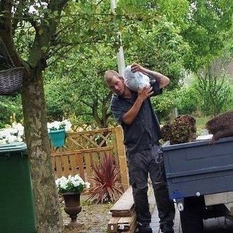 Een man draagt ​​een groot, wit voorwerp op zijn schouder, buiten in de buurt van een kleine vrachtwagen.