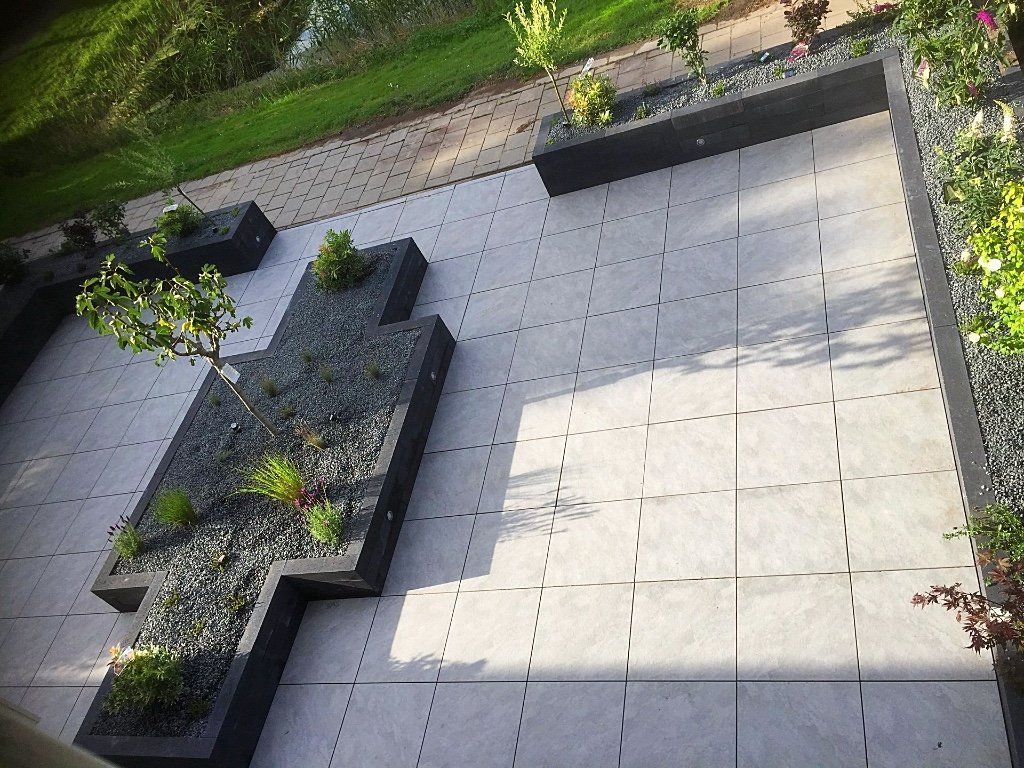 Modern terras met grijze natuurstenen tegels, donkere plantenbakken en groen.