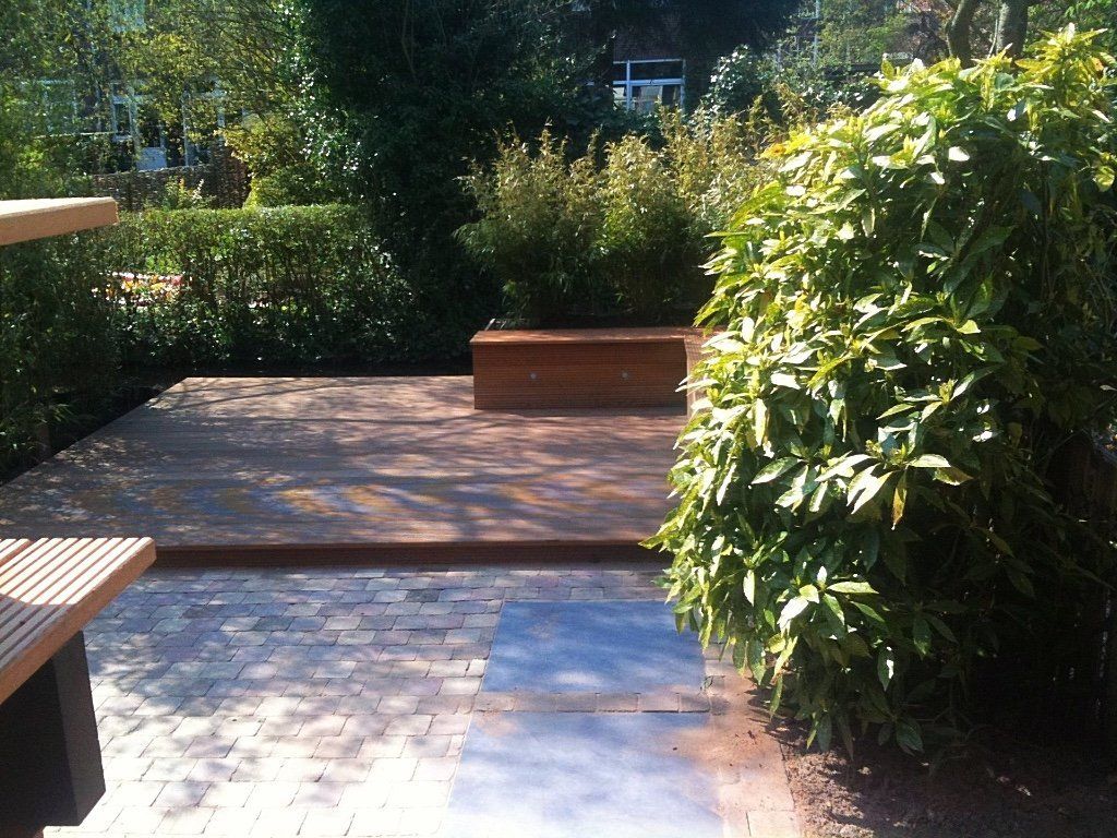 Houten terras met banken en struiken in een tuinachtige omgeving.