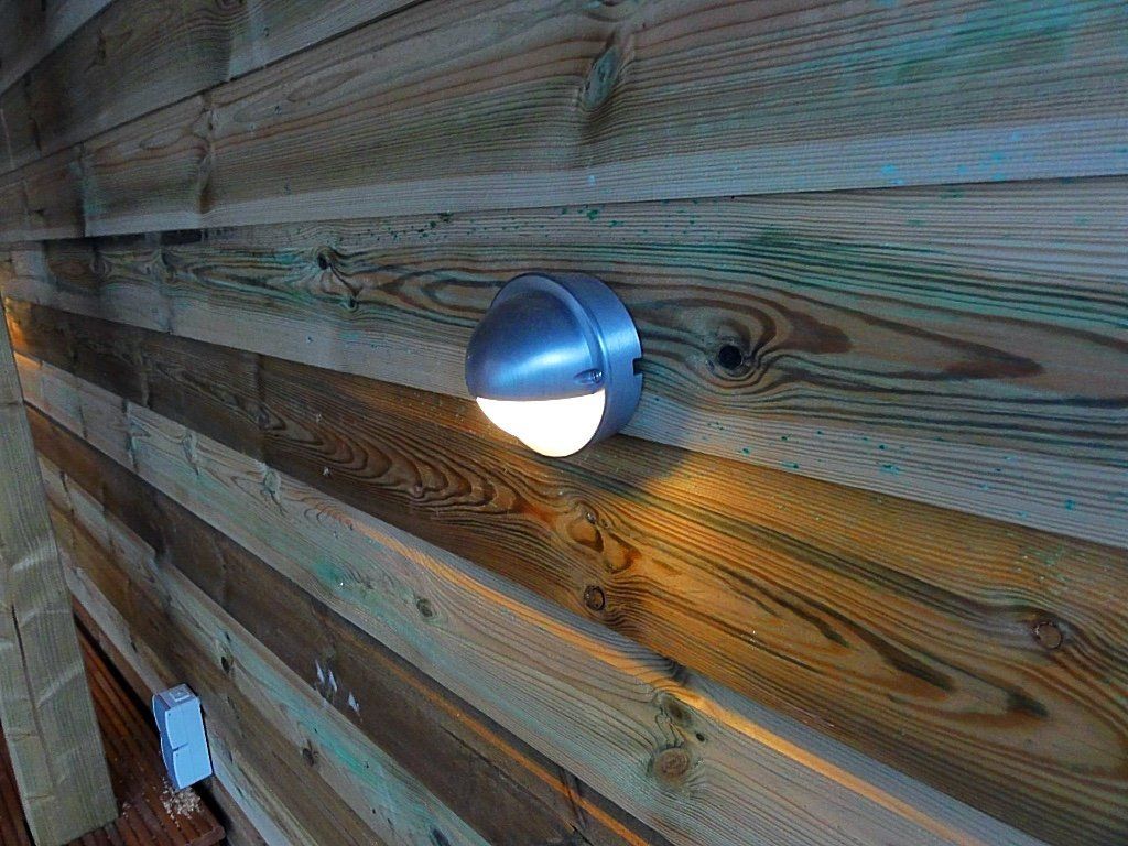 Buitenlamp gemonteerd op houten planken, die een warme gloed verspreidt.