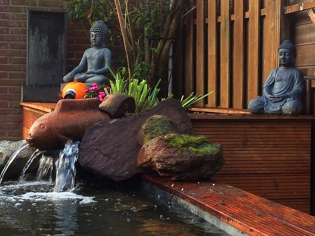 Waterpartij met Boeddhabeelden, waterval, rotsen en een houten vlonder.