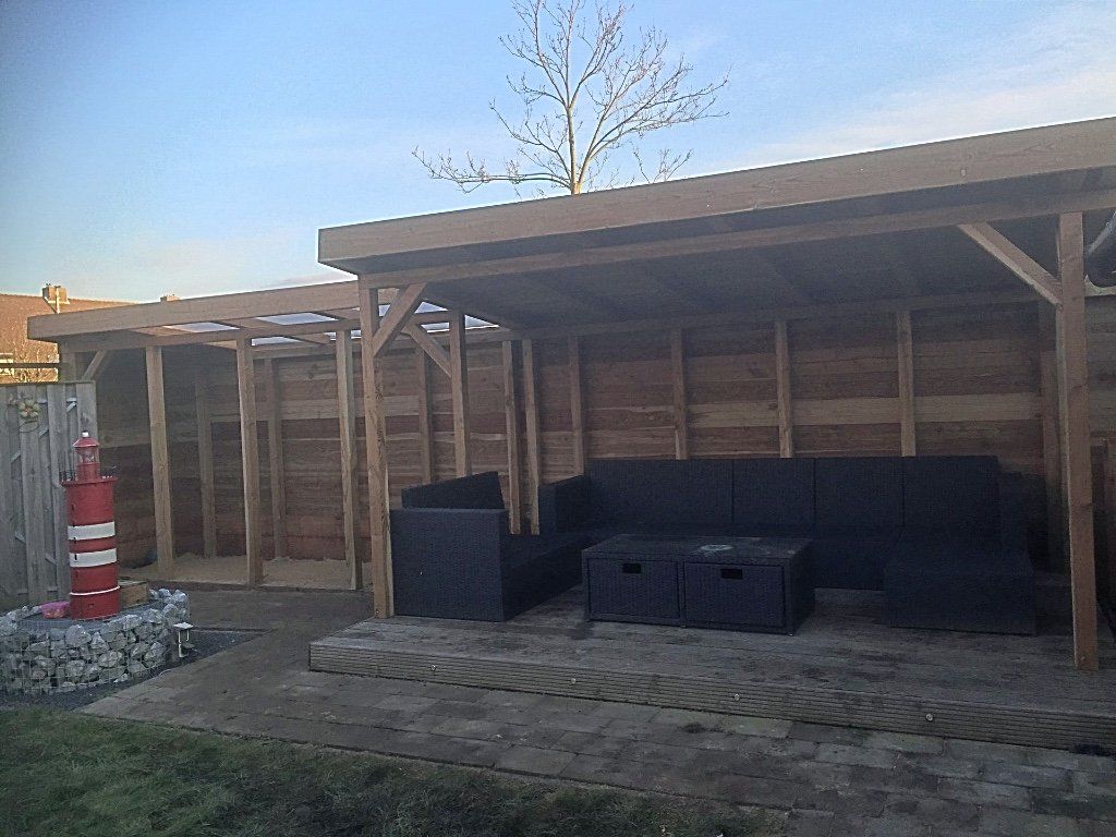 Houten zithoek buiten met een zwarte bank, een salontafel en een rode vuurtorendecoratie.