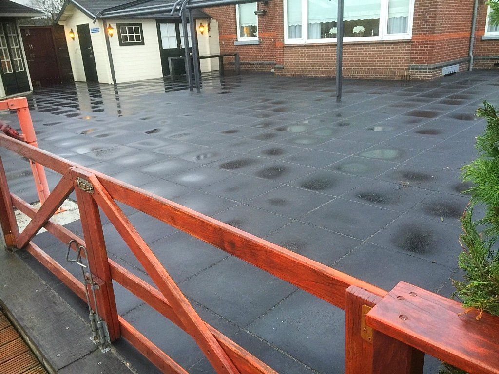 Rode poort voor een natte, donker betegelde buitenruimte. Op de achtergrond is een gebouw te zien.