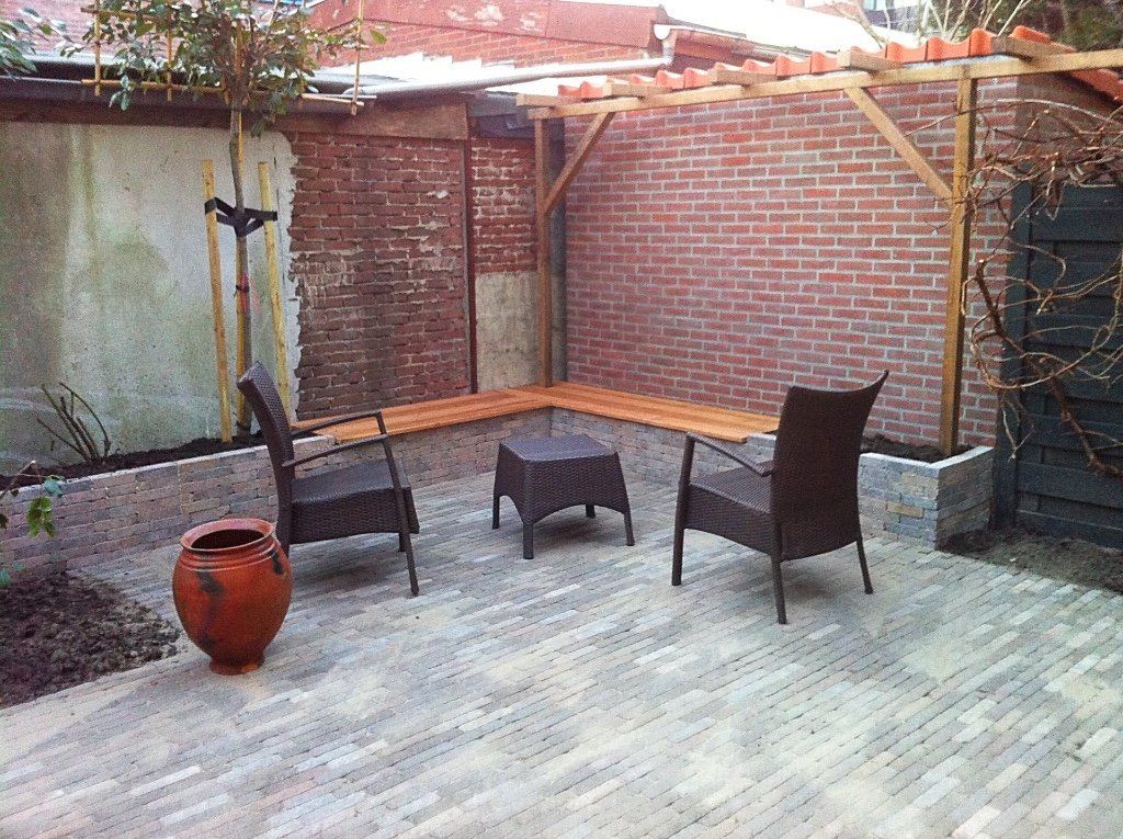 Buitenpatio met bakstenen muren, houten pergola, zitgelegenheid en een grote terracotta pot.