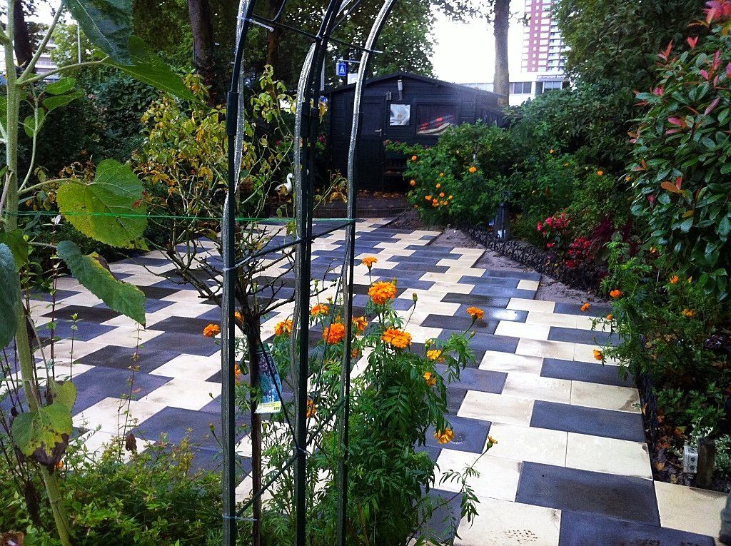 Tuinpad met zwart-witte tegels, oranje bloemen en weelderig groen.