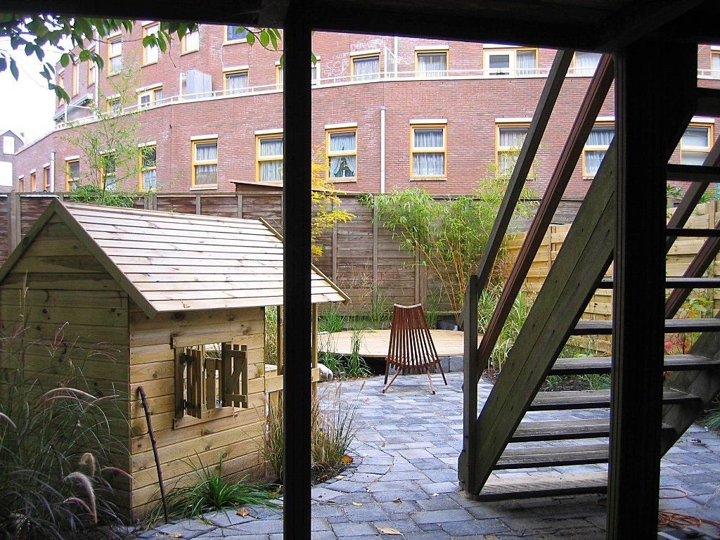 Achtertuin met houten speelhuisje, trap en een bakstenen gebouw als achtergrond.