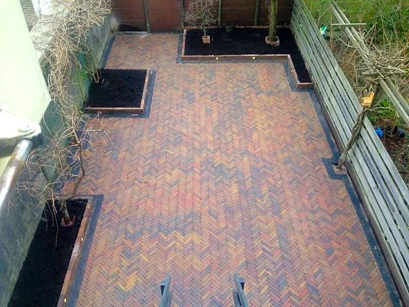 Een stenen terras met twee verhoogde plantenbakken en een schutting.