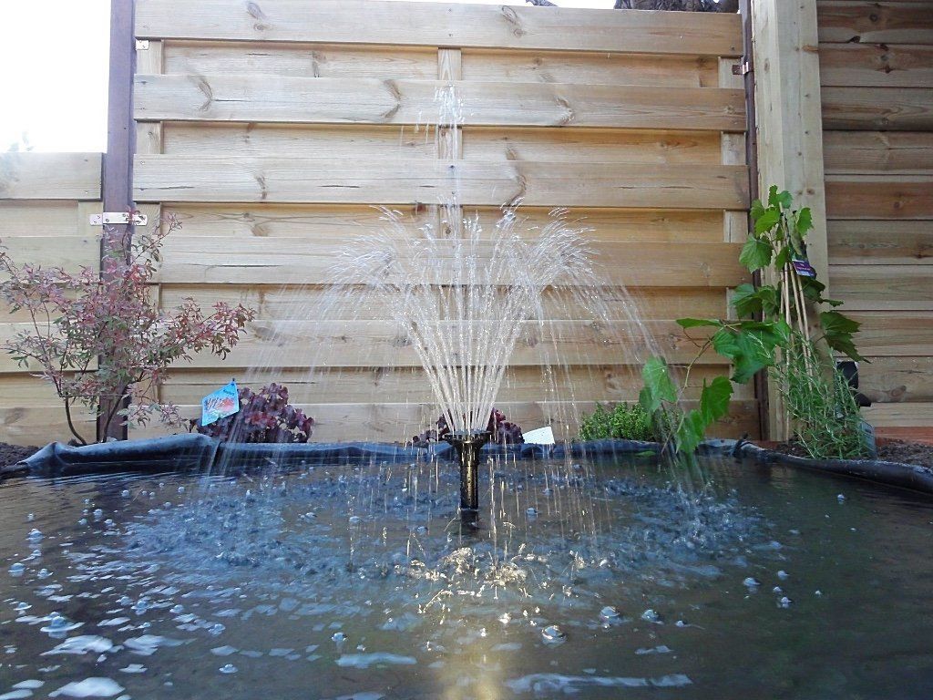 Een waterfontein sproeit water in een kleine vijver tegen een houten schutting.