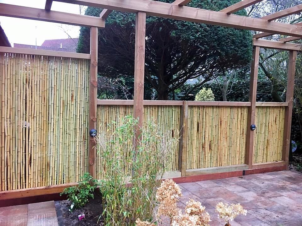 Houten pergola met bamboe schutting, in een tuinomgeving.