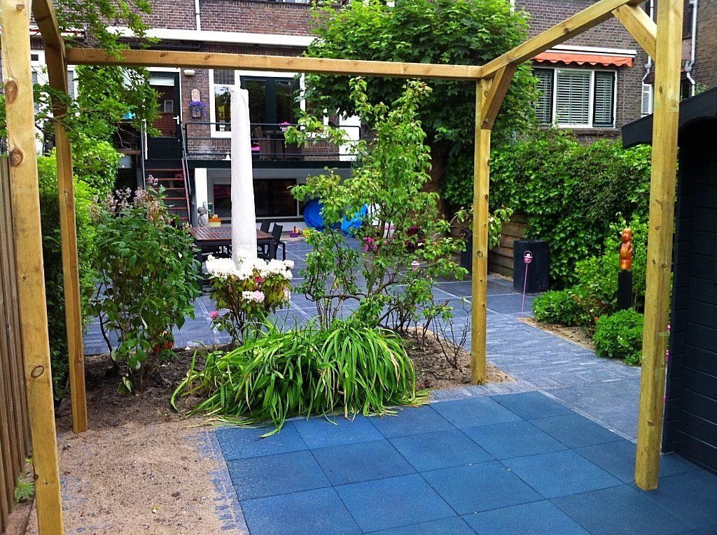 Een houten pergola boven een tuin met een blauwe tegelvloer en weelderig groen.