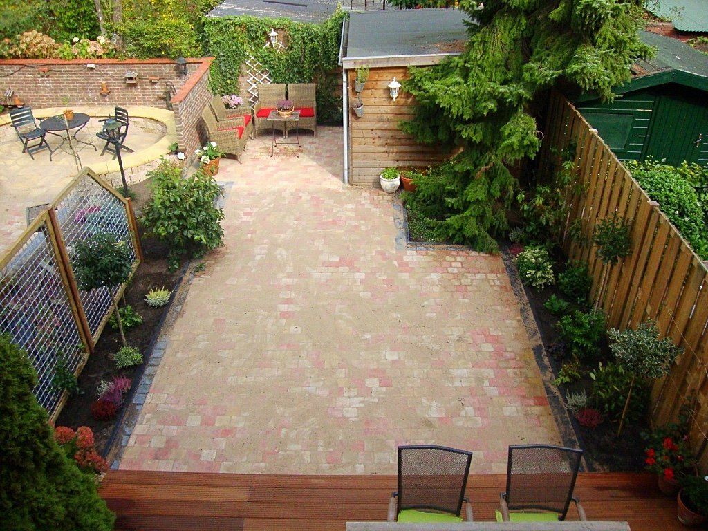 Terras in de achtertuin met bakstenen bestrating, zitjes en omringende beplanting.