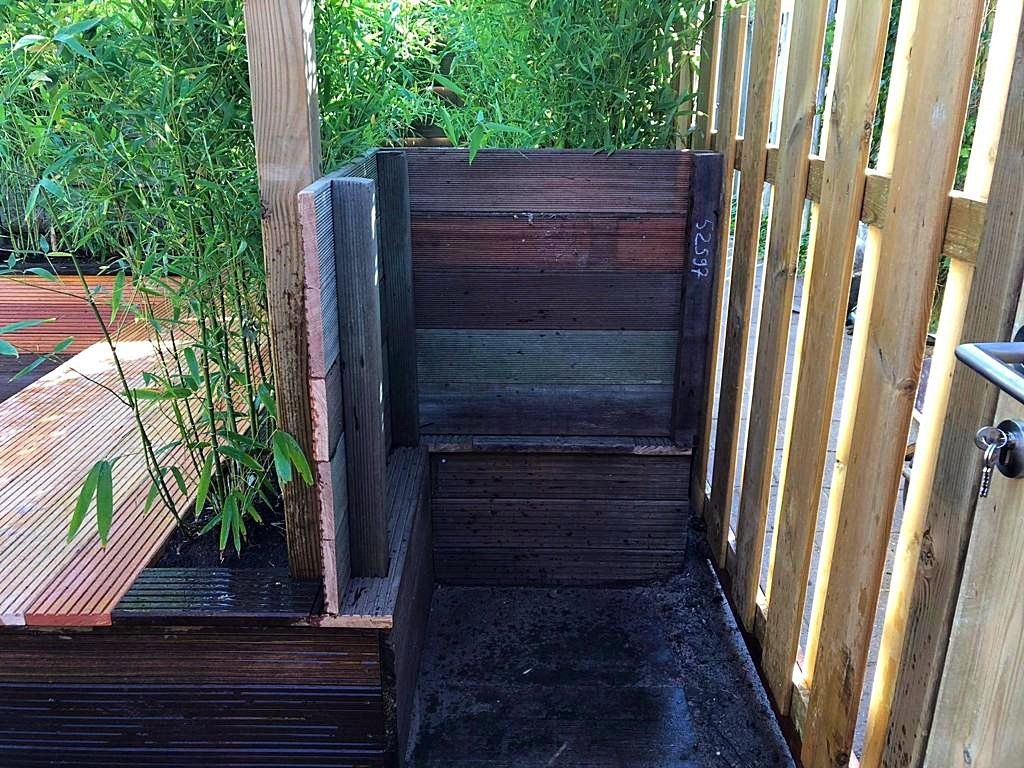 Een houten compostbak naast een houten schutting en groen.