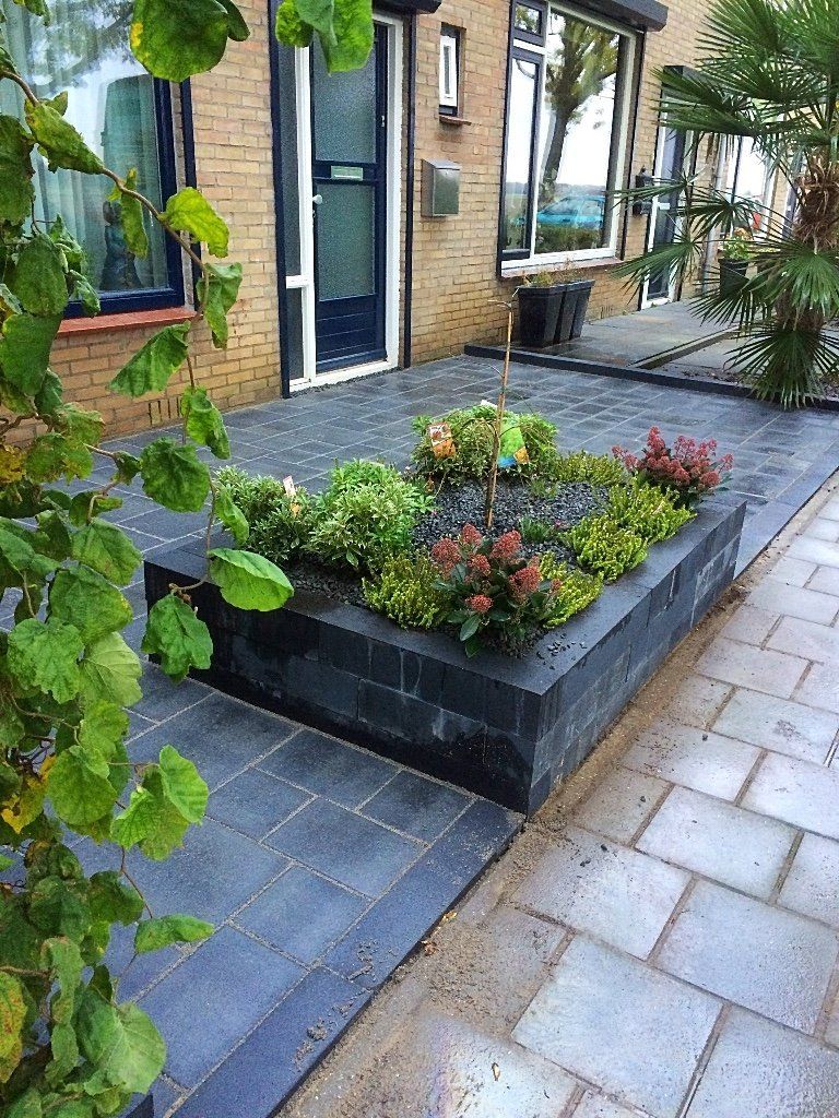 Verhoogd bloembed met kleurrijke bloemen en struiken voor een bakstenen gebouw.