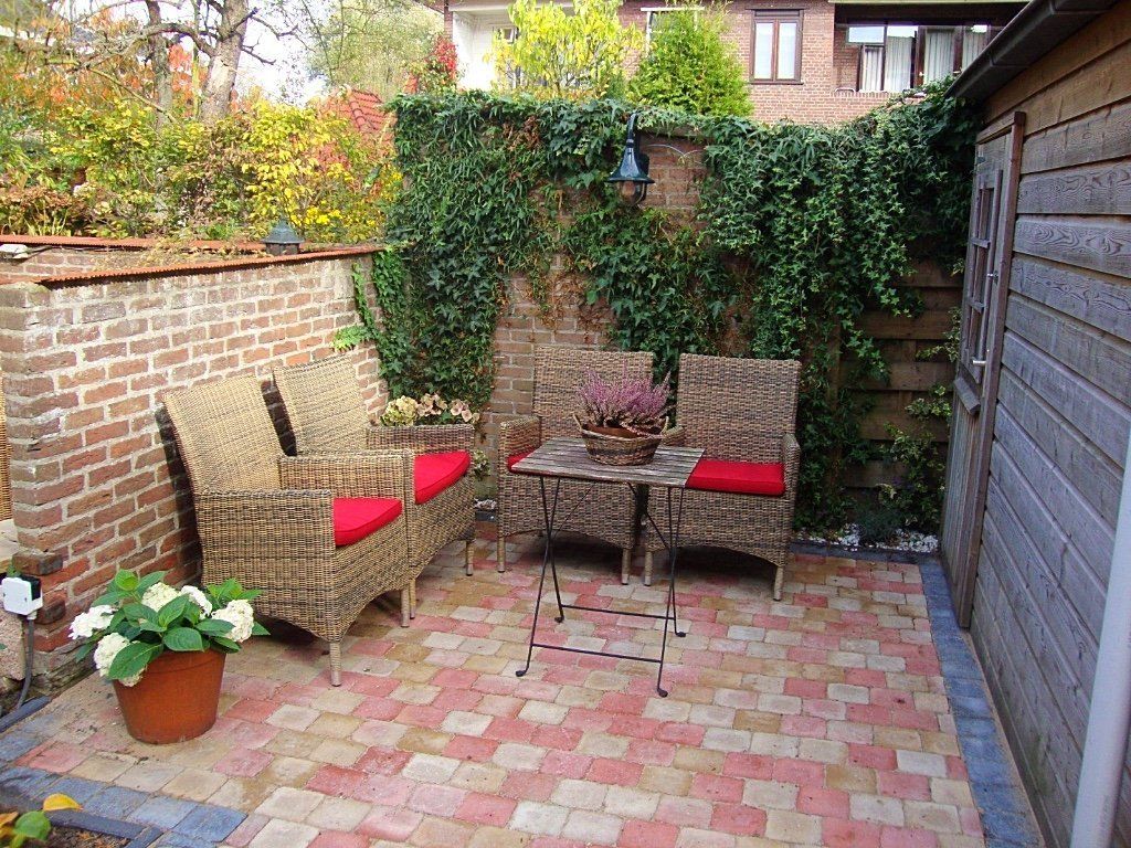 Gezellig terras buiten met bakstenen muren, gevlochten stoelen met rode kussens, een klein tafeltje en klimop.